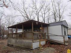 a small house with a porch in the middle of some trees and leaves on the ground