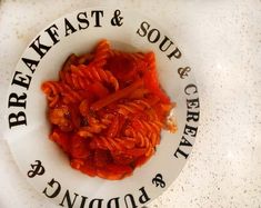 a white plate topped with pasta and sauce on top of a marble counter next to a sign that reads breakfast & soup & craft