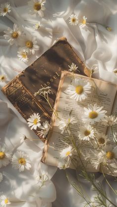 an open book laying on top of a bed covered in white daisies and flowers