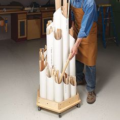 a man in an apron standing next to a large stack of pipes with wooden handles