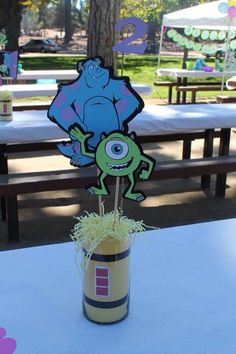 a table topped with a vase filled with grass and a cut out of a frog sitting on top of it