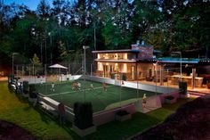 an aerial view of a tennis court at night with people playing on the grass in front of it