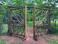 two wooden gates made out of branches in the middle of a field with grass and trees behind them