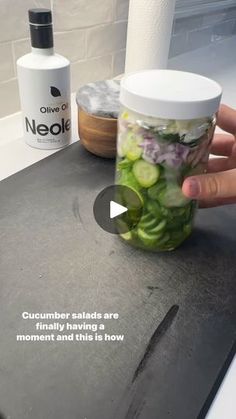 a person holding a jar filled with cucumbers on top of a kitchen counter