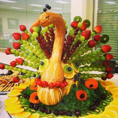 a fruit sculpture made to look like a peacock with grapes and oranges around it