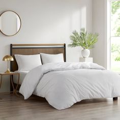 a bed with white sheets and pillows in a room next to a table with a potted plant