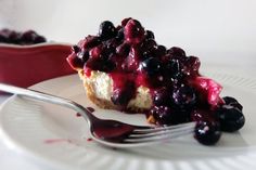 a piece of cheesecake with blueberries and sauce on a plate next to a fork