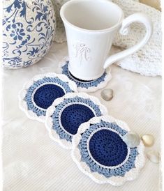 three crocheted coasters sitting on top of a table next to a coffee cup