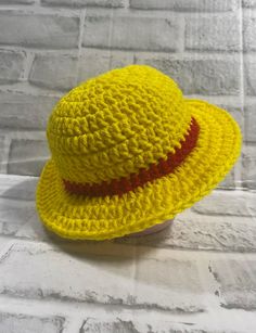 a crocheted yellow hat sitting on top of a white brick wall next to a cup