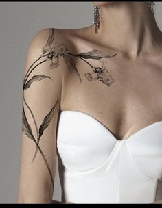 a woman wearing a strapless white dress with flowers on her arm and shoulder tattoo