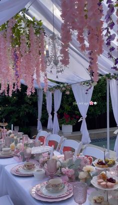 the table is set with tea cups and saucers, plates and flowers hanging from the ceiling