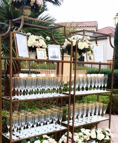 there are many wine glasses on the shelves in front of some flowers and greenery