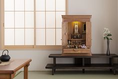 a wooden cabinet sitting on top of a table next to a vase with flowers in it