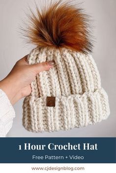 a hand holding a white knitted hat with brown fur pom - pom