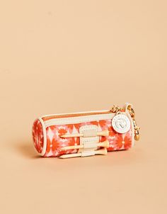 an orange and white flowered purse on a beige background with a gold keychain