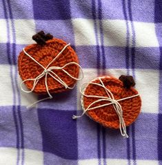 two crocheted pumpkins sitting on top of a purple and white checkered blanket