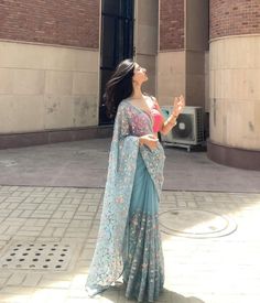 a woman in a blue sari is standing on the sidewalk and looking up at something