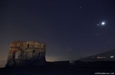 the moon is shining over an old castle