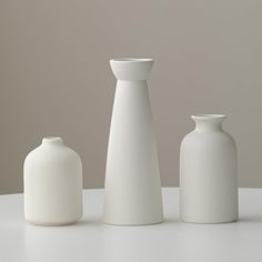 three white vases sitting on top of a table