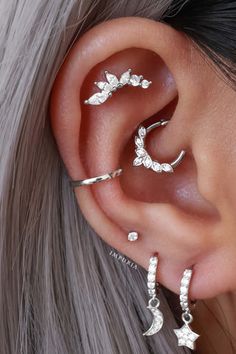 a woman's ear with three silver stars and moon piercings on the side