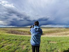 a person standing on top of a grass covered field holding a camera up to the sky