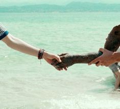 two people reaching out to each other in the water with their hands over another person's arm