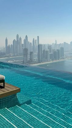 an outdoor swimming pool in front of a large cityscape with the ocean and skyscrapers