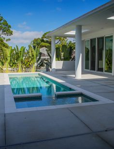 an empty swimming pool in the middle of a house with trees and bushes around it