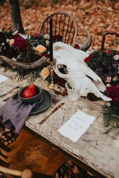 the table is set with an antelope skull, flowers and fruit on it