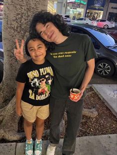 a man standing next to a little boy in front of a tree with his peace sign