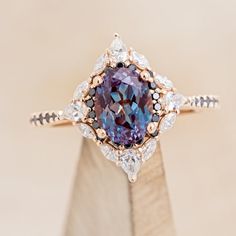 a fancy ring with a purple diamond surrounded by white and black diamonds on a wooden stand