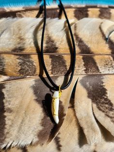 a necklace with a cow hide pattern and a long horn pendant on a black cord