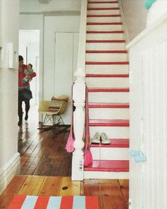 a red and white striped rug on the floor in front of a stair case with a woman holding a baby