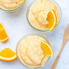 three small glass bowls filled with oranges and whipped cream next to a wooden spoon