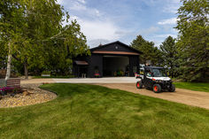 a tractor is parked in front of a garage on the side of a dirt road