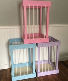 three different colored bird cages sitting on top of a wooden floor