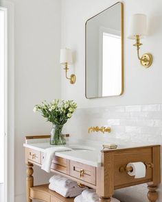 a white bathroom with gold fixtures and flowers on the sink counter, next to a mirror