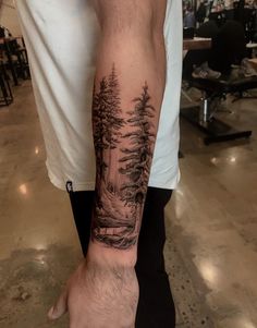 a man's arm with a forest scene tattoo on the left side of his arm