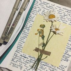 two pens are sitting on top of an open notebook with flowers and writing paper next to it