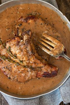 a pan filled with meat and gravy on top of a wooden table next to a fork