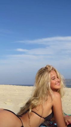 a beautiful woman laying on top of a beach next to a surfboard in the sand