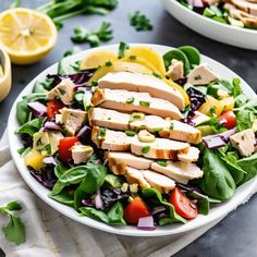 a salad with chicken, lettuce, and tomatoes on a plate next to a bowl of dressing