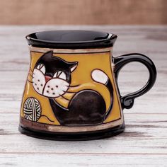 a black and yellow coffee mug with a cat on it's side sitting on a wooden table