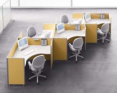 an office cubicle with four chairs and two computer screens on the desks, all in different colors