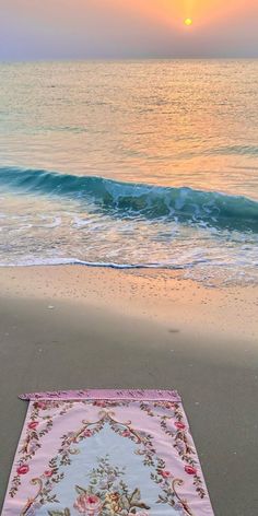 a blanket laying on the beach in front of the ocean at sunset with waves coming in