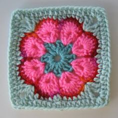 a crocheted square with a pink and blue flower in the center on a white surface