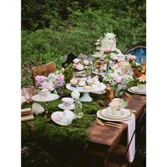 a table with plates and flowers on it in the middle of a forest filled with trees