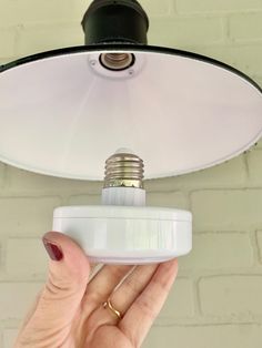 a person holding a light bulb in front of a white brick wall and ceiling fixture