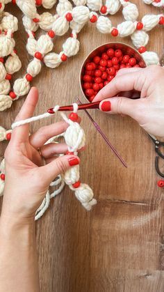 two hands crocheting red and white beads on a piece of wood with scissors