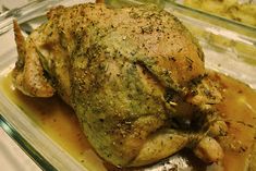 a roasted chicken in a glass dish with gravy on the bottom and sides